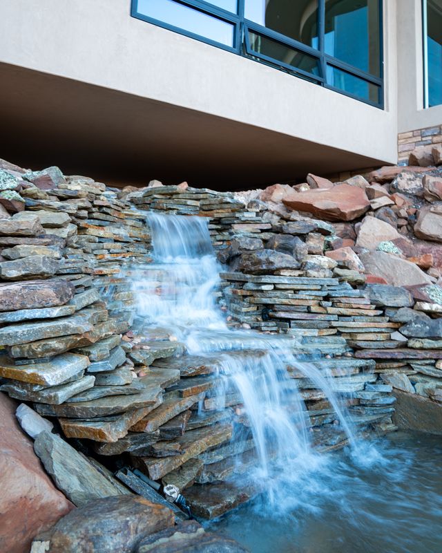 Stacked flagstone waterfall cascading into a pond beneath a modern home