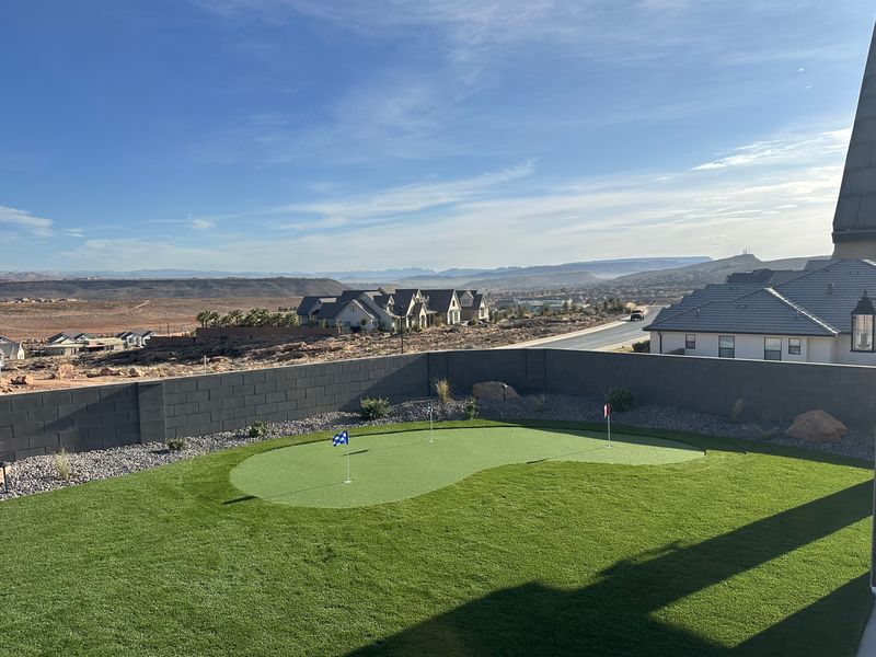 Turf backyard with a kidney-shaped putting green and flags inside a block wall, with a view of the valley and mesas
