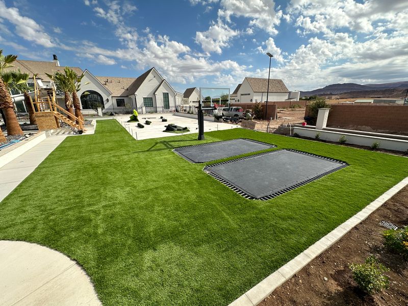 Large artificial turf backyard with two in-ground trampolines and a basketball hoop, installation in progress