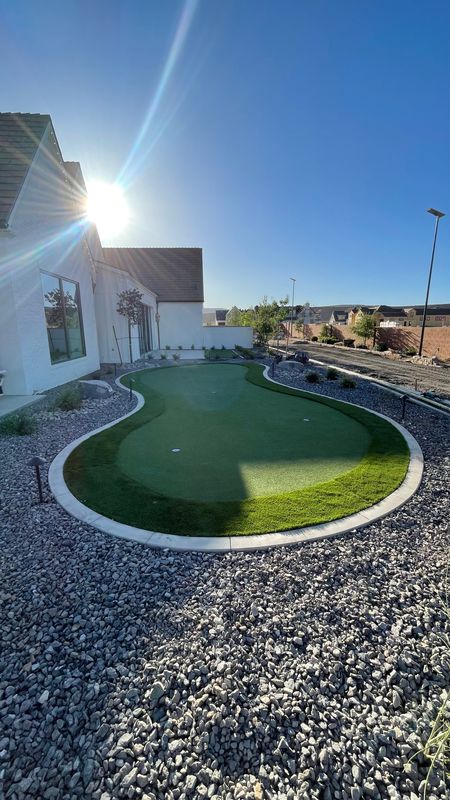 Artificial turf putting green with concrete curbing, surrounded by rock and landscape lights